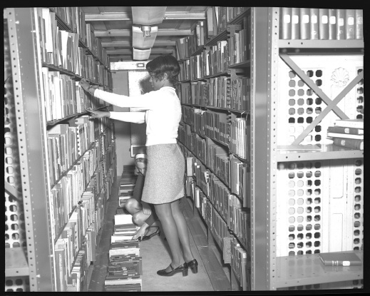 Crowded stacks, 1970. Photograph shows an African American employee of the Library of Congress among crowded book shelves with another employee. Photo courtesy Library of Congress Prints and Photographs Division Washington, D.C. https://www.loc.gov/item/2017646178/